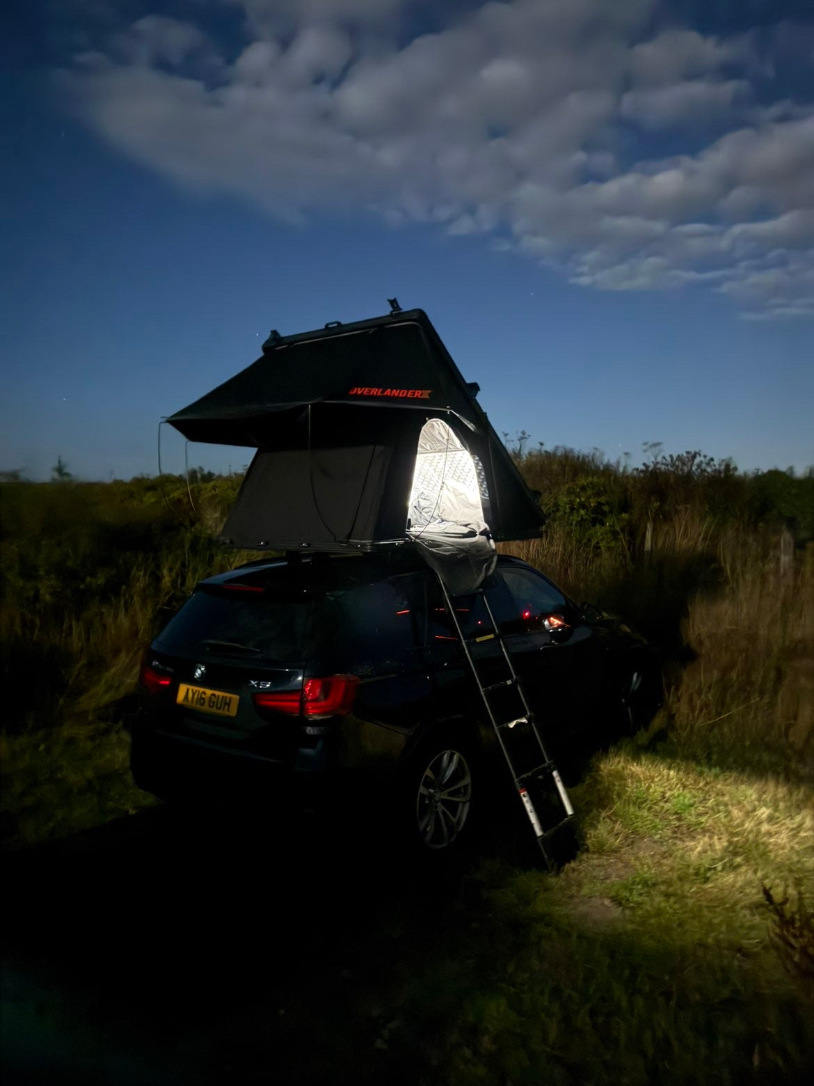 OverlanderX clamshell rooftop tent illuminated at dusk on a dark SUV