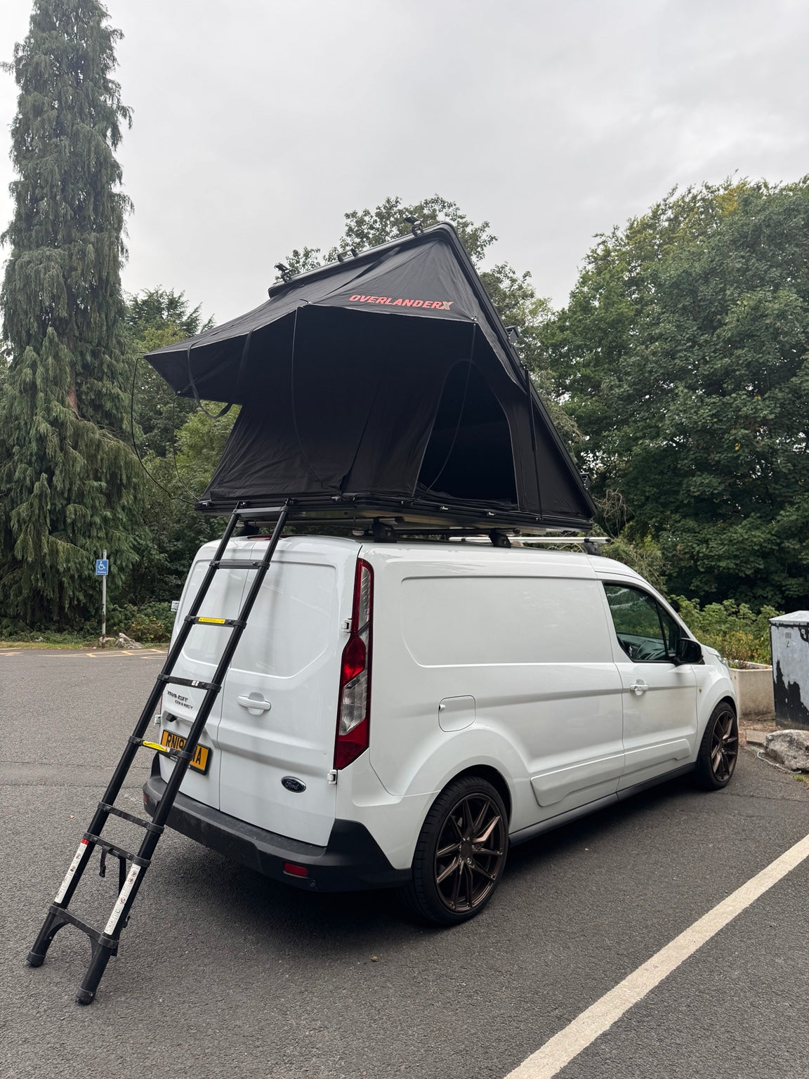 Rear view of an open OverlanderX rooftop tent and telescopic ladder on a white van