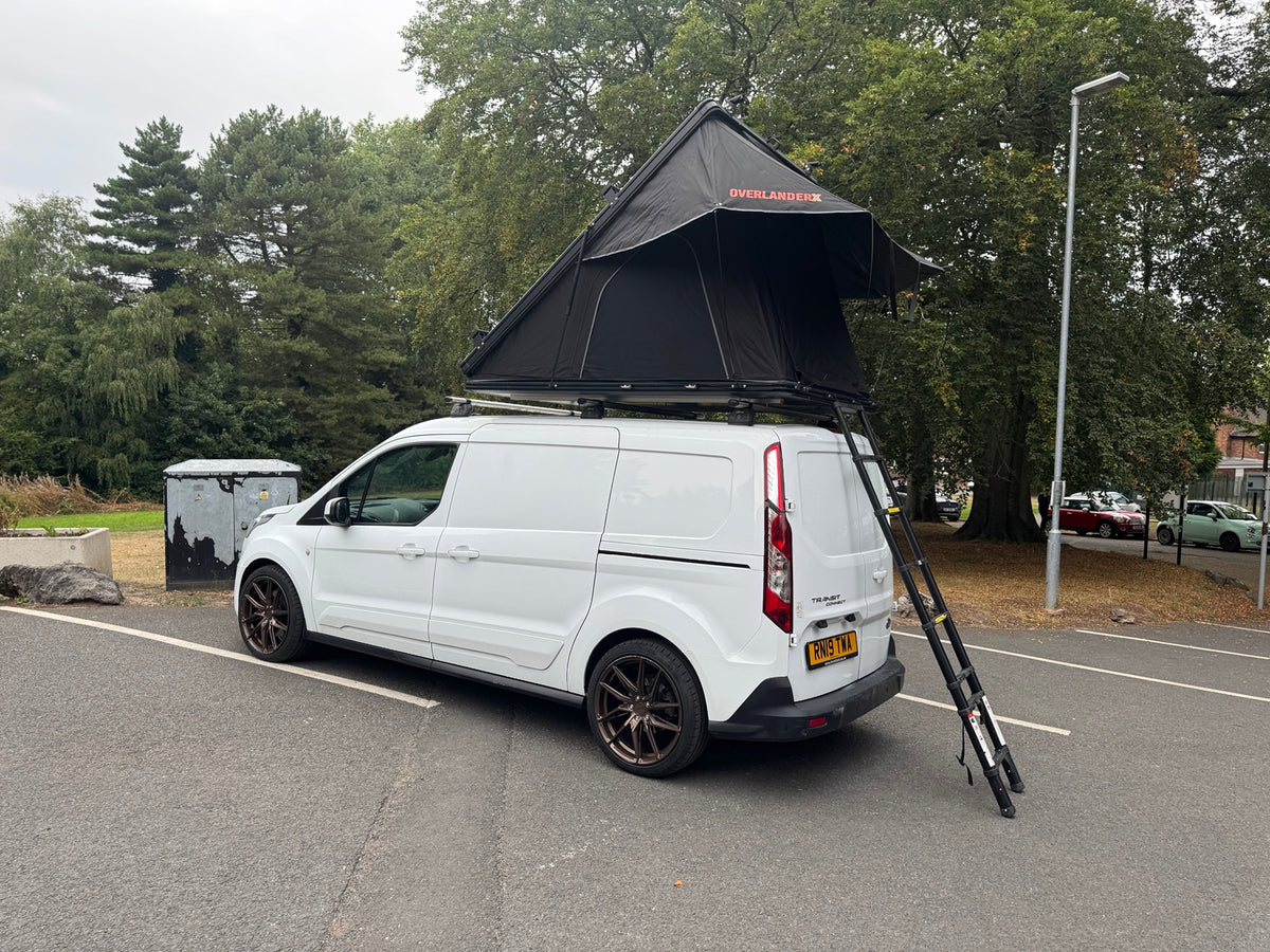 OverlanderX clamshell rooftop tent open on a white van, with ladder beside trees