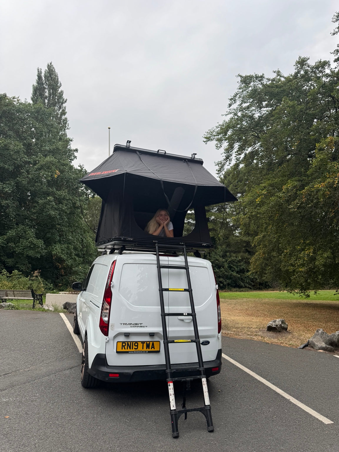 Person relaxing in an open OverlanderX rooftop tent on a white van
